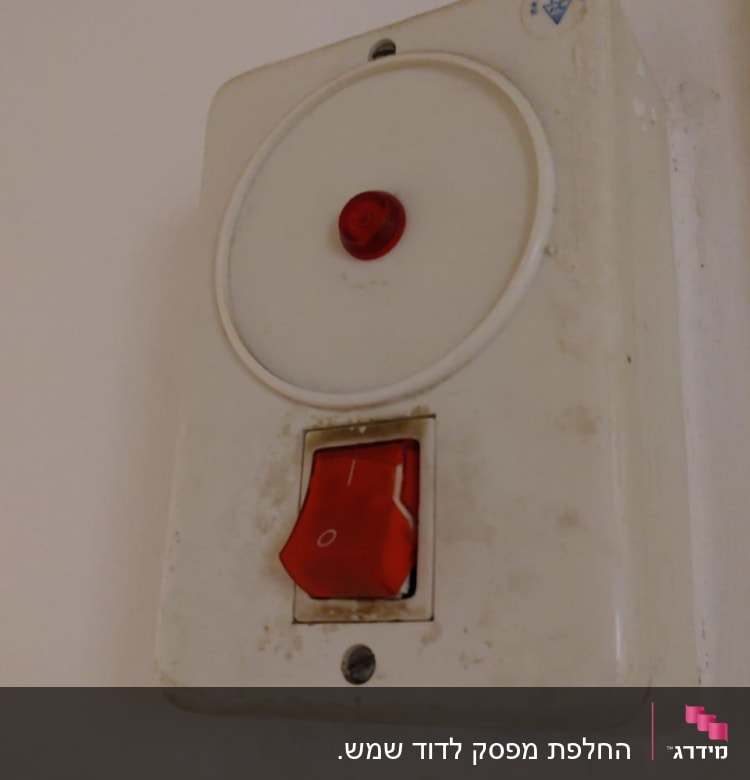 מתג חשמלי עם כפתור אדום על קיר לבן